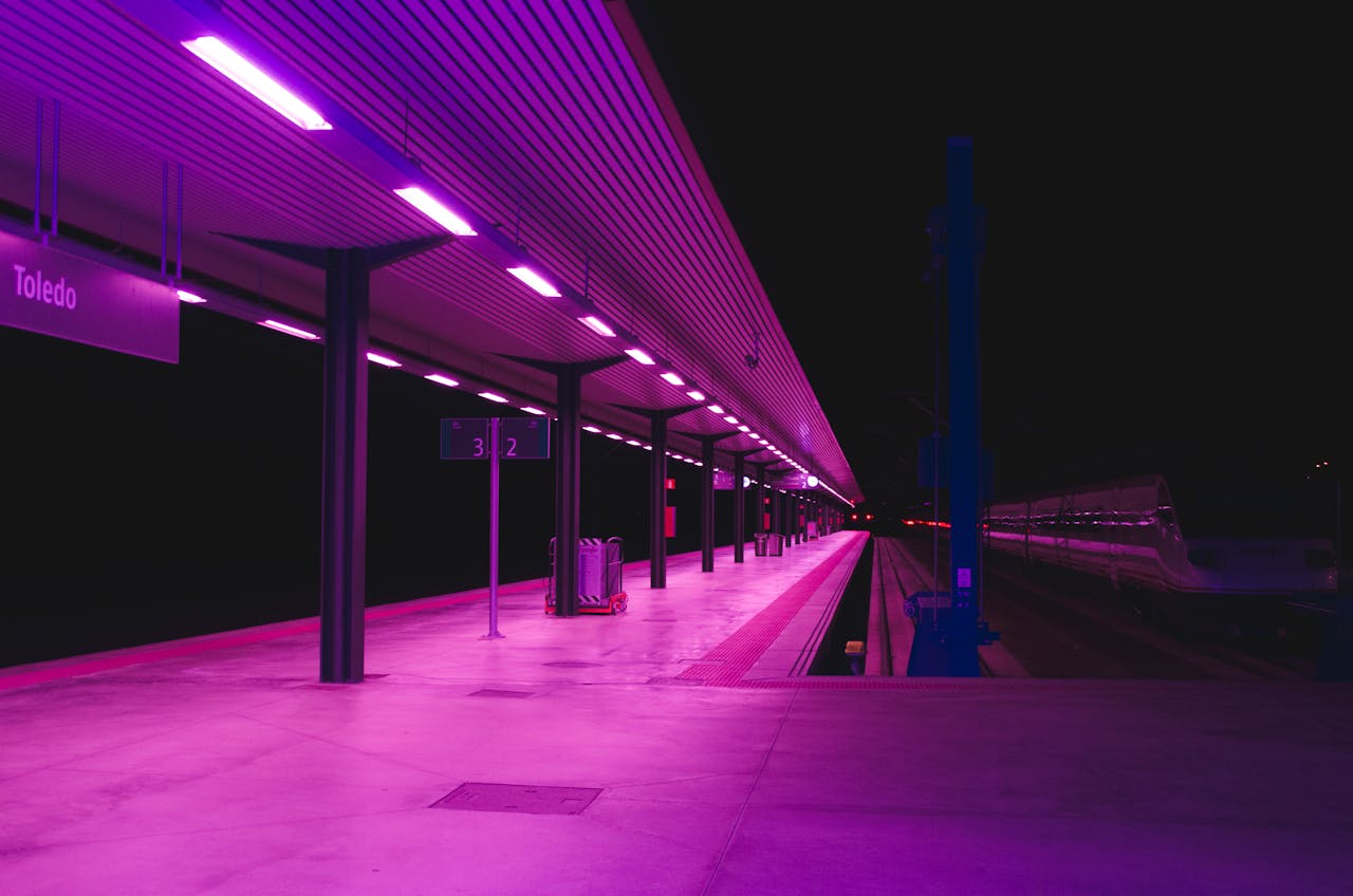 Explore the vibrant neon-lit train station platform in Toledo at night, showcasing urban architecture.